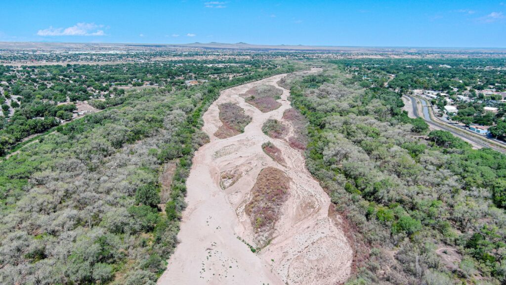 An aerial image of a dry riverbed with browning riparian vegetation on either side.