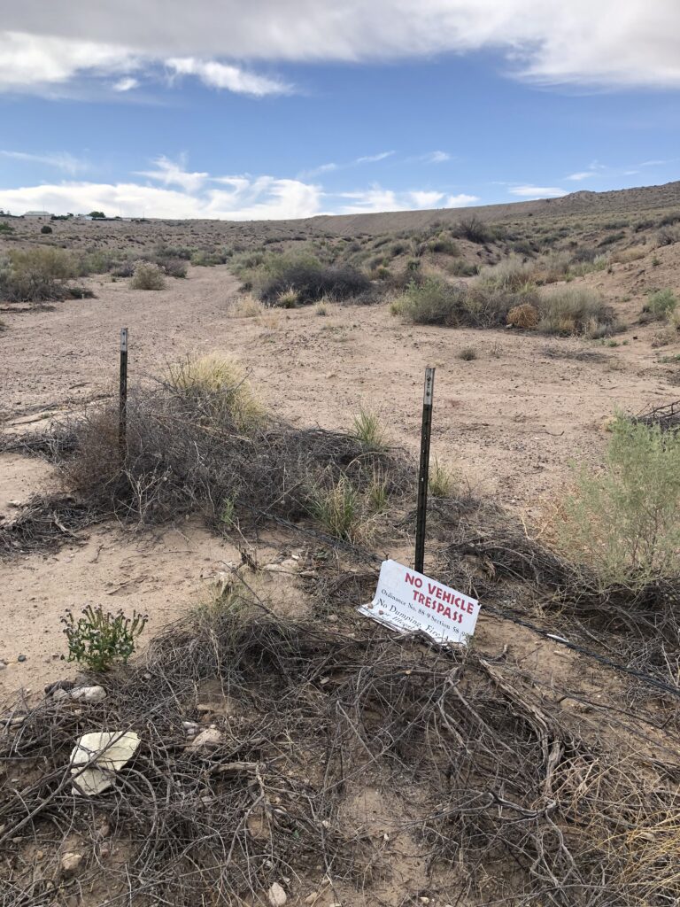Fallen down “No Vehicle Trespass” sign on a barbed wire fence with a desert arroyo.