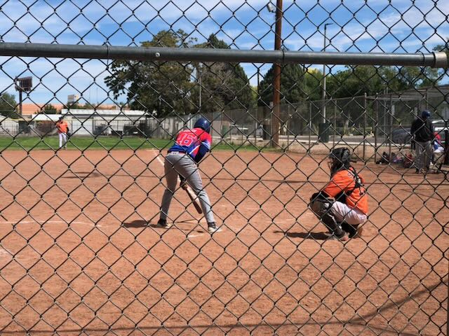 Two baseball players behind a chain link fence - a batter leaning over and tapping the plate with his bat and a catcher crouched waiting for the pitch.