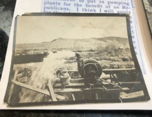 Black and white picture of an old pump, pumping water into an irrigation ditch.