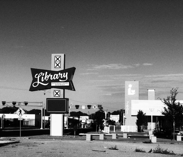 Black and white photograph of a library with "library" sign and a street beyond
