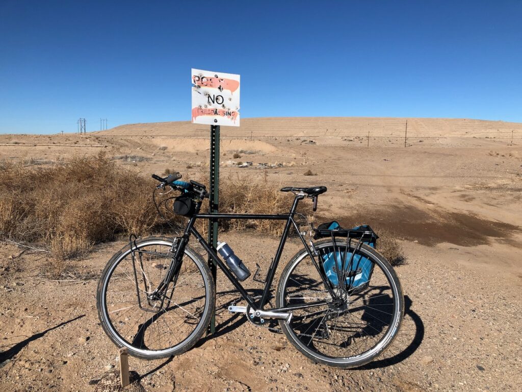 Bicycle leaning against a "no trespassing" sign with open desert behind