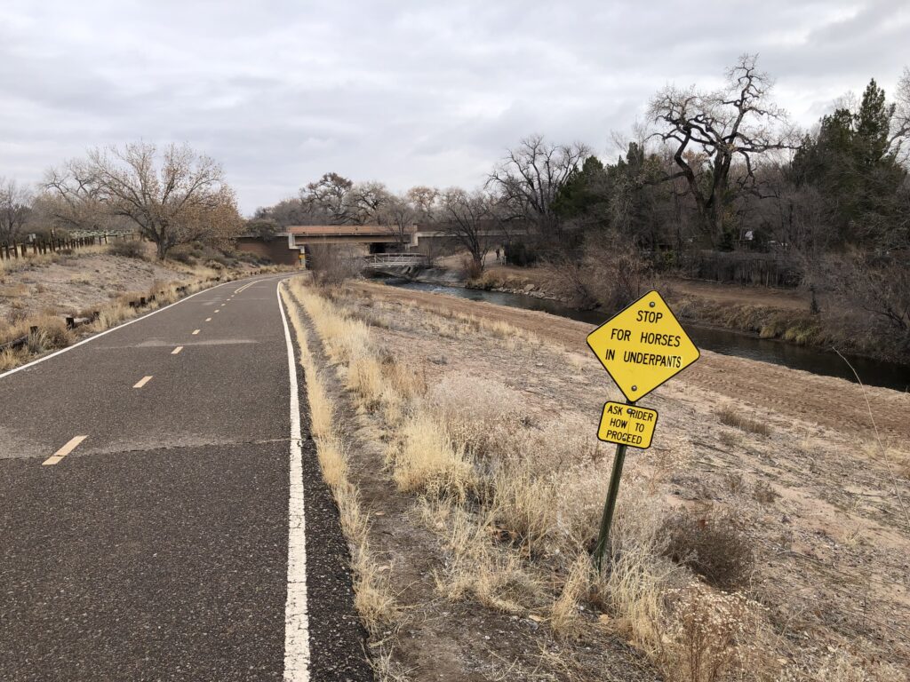 Bike trail with yellow warning sign reading “Stop for Horses In Underpants”. It appears to be an alteration.