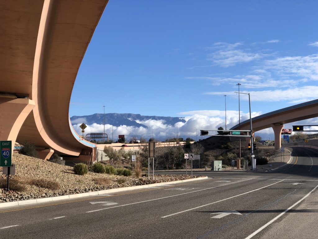 Distant mountains, with clouds hanging below the mountaintops, and sweeping freeway overpasses.