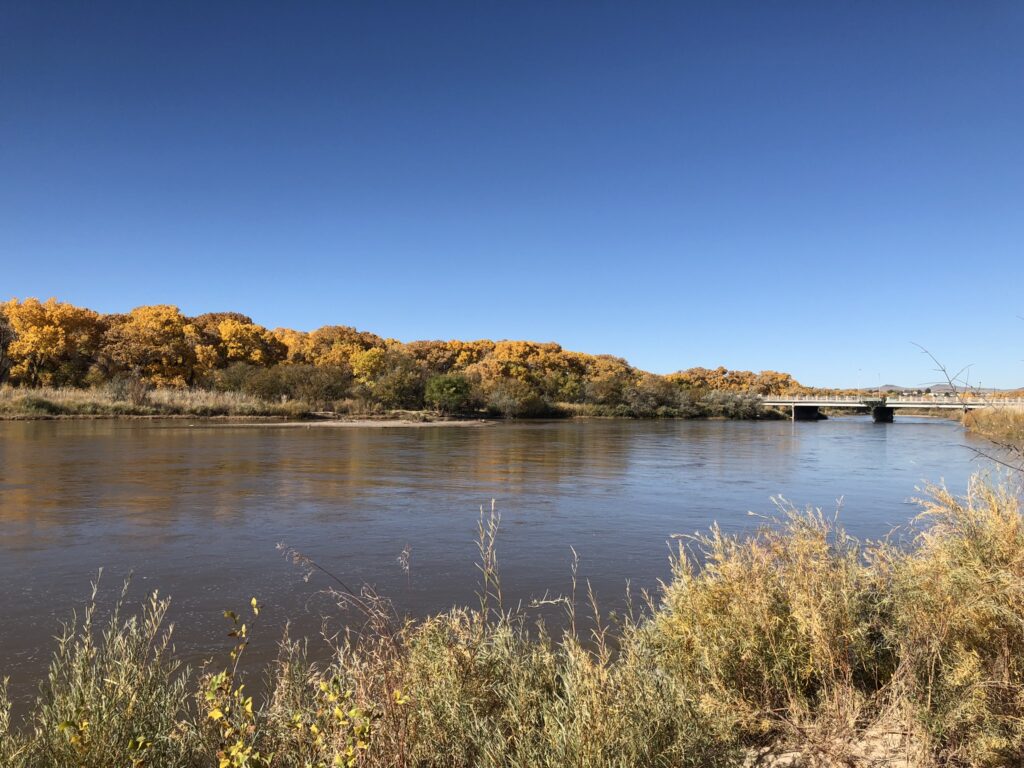 A river with fall colored-trees in the background and a bridge.