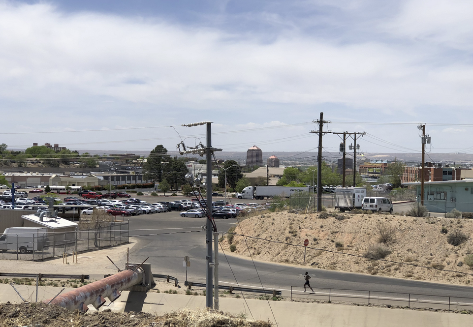 Roadway with parked cars, power lines, and downtown Albuquerque buildings in the distance