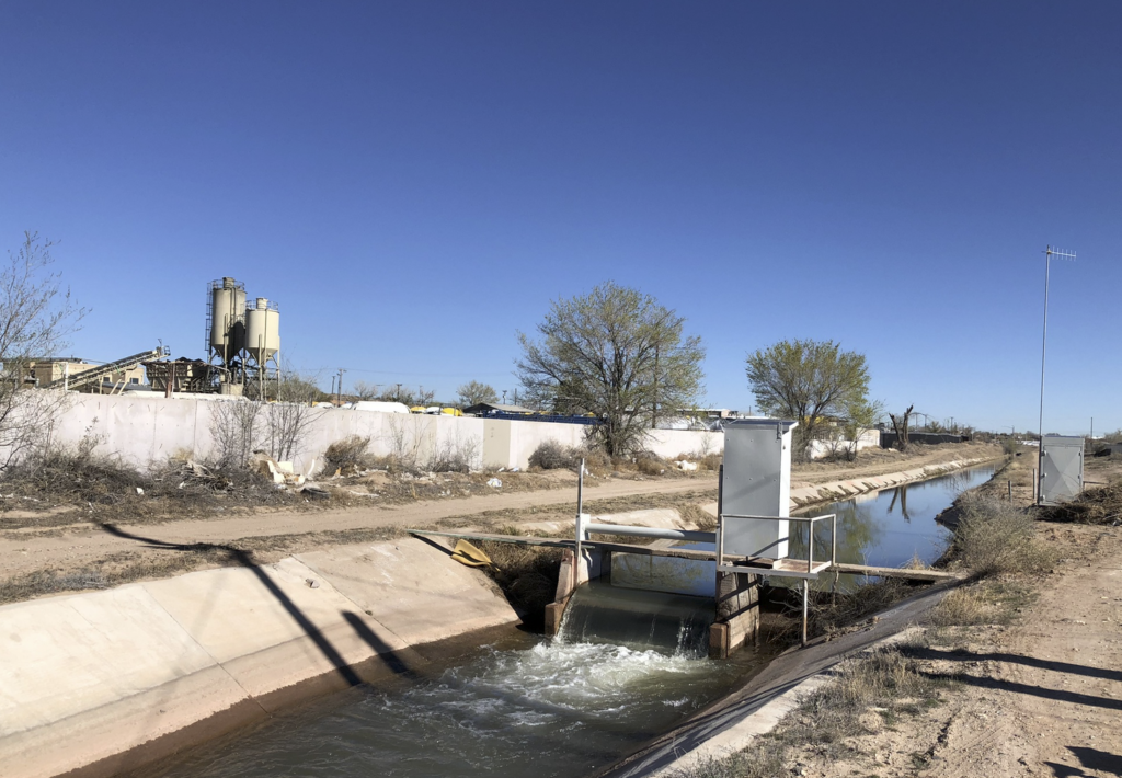 Irrigation canal with cement plant in the background.